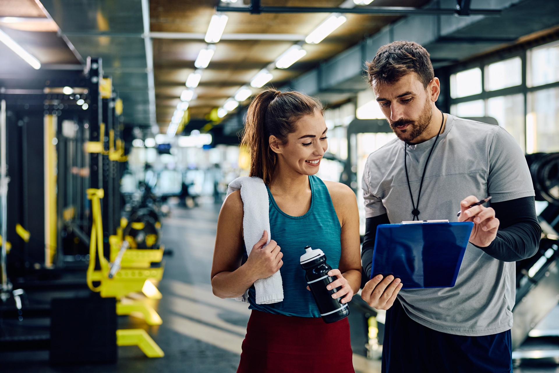 Happy sportswoman and her fitness instructor analyzing workout plans in health club.