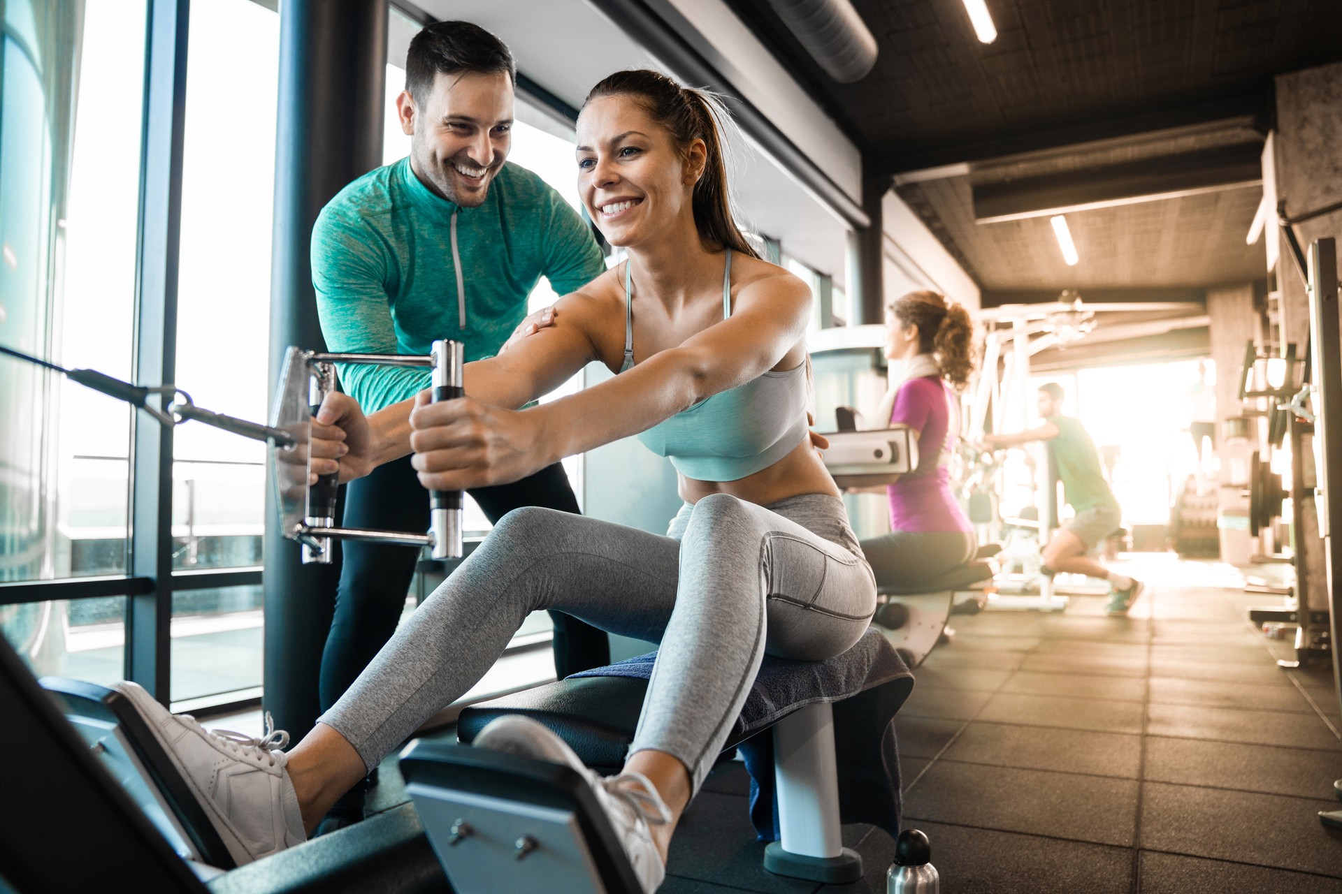 Happy female athlete doing rowing workout with personal trainer in the gym